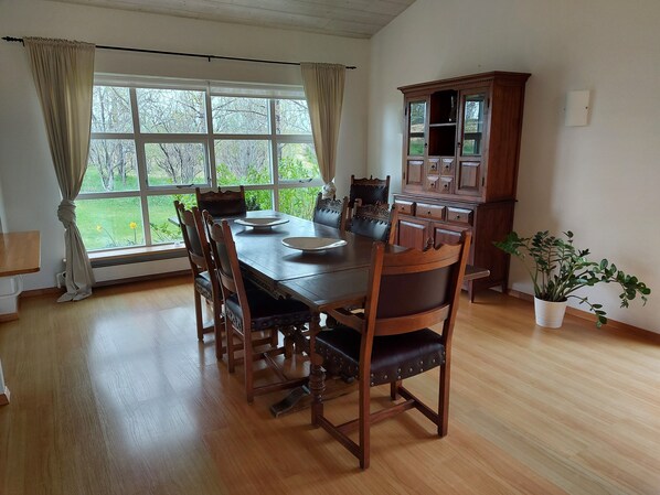 A dining area with a wooden table and chairs, a cabinet, and a window with curtains. - Hótel Skálholt (Bláskógabyggd)