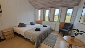 A bedroom with two beds, a chair, a small table, and large windows. - Hótel Skálholt (Bláskógabyggd)