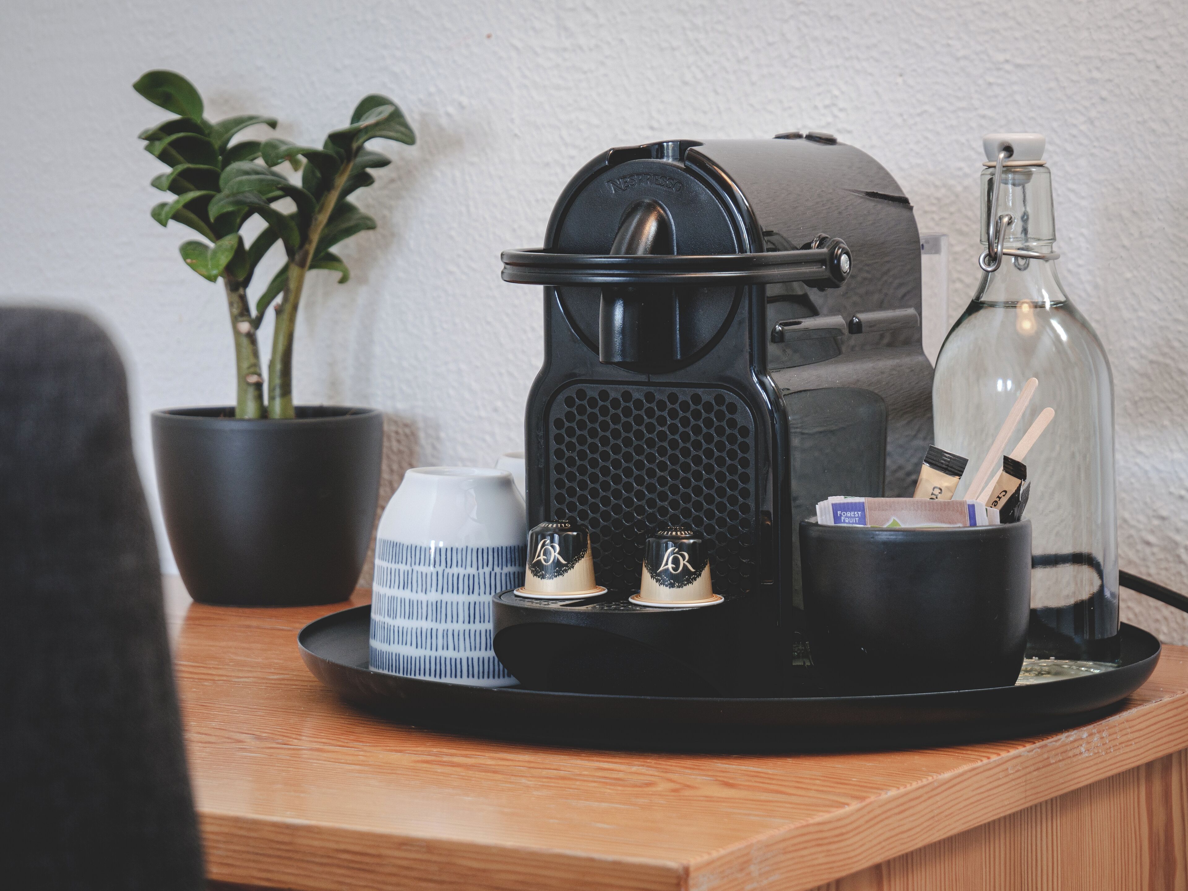 A coffee machine on a tray with a plant, a cup, and a bottle.