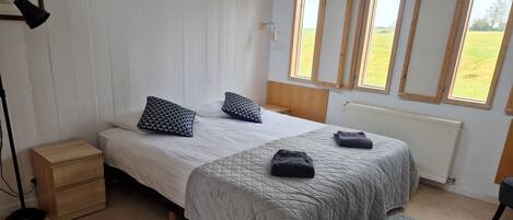 Ein Schlafzimmer mit Bett, Nachttischen, einem Heizkörper und großen Fenstern.