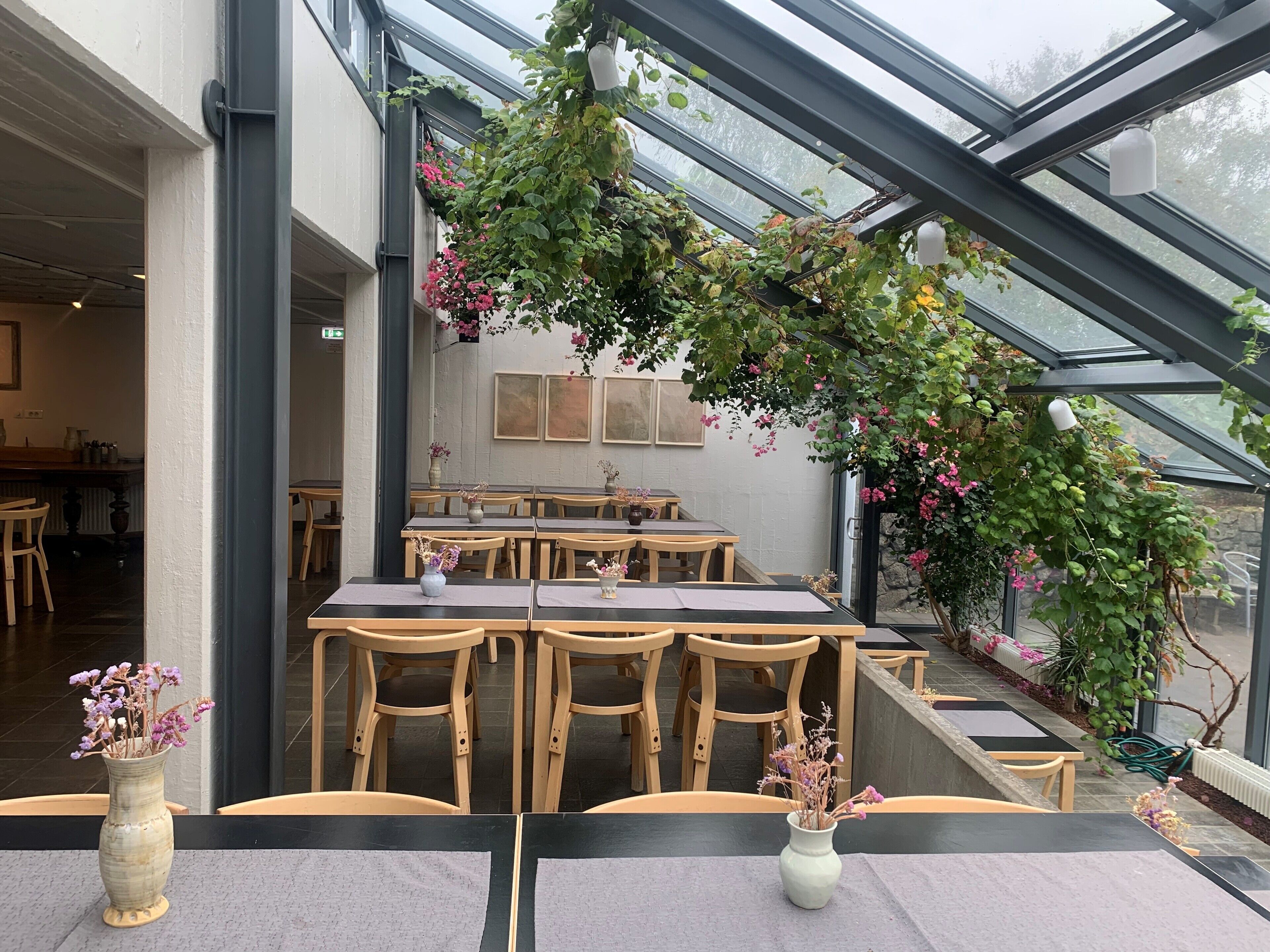 Un espace de restauration intérieur avec des tables et des chaises en bois, un plafond en verre et des plantes en pot.