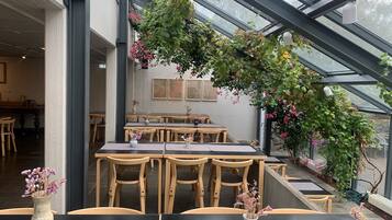 Un espace de restauration intérieur avec des tables et des chaises en bois, un plafond en verre et des plantes en pot.
