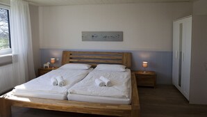 Ein Doppelbett mit zwei Kissen und zwei gerollten Handtüchern, ein hölzernes Kopfstück, Nachttische mit Lampen, ein Bild an der Wand und ein Kleiderschrank.