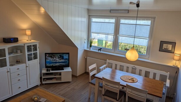 Ein gemütliches Zimmer mit einem Holzespeisetisch, weißen Stühlen, einem Fernseher und einem Fenster mit Aussicht.