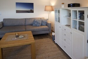 Ein Wohnzimmer mit grauem Sofa, einem Holztisch, einer Lampe und einer Vitrine.