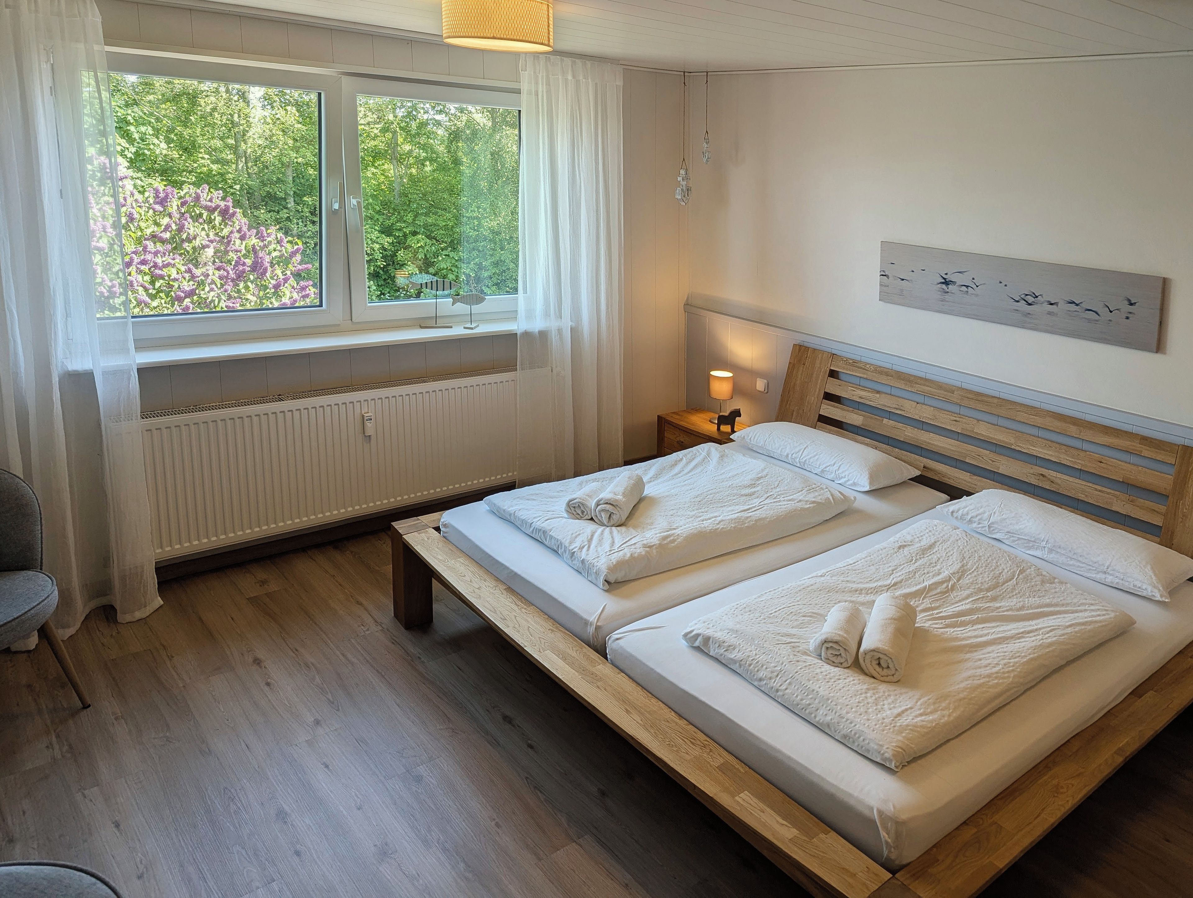 A bedroom with a double bed, a bedside table with a lamp, a window with curtains, and a radiator.