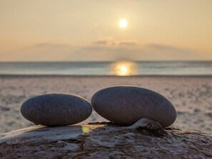Two smooth stones balanced on a wooden surface with a calm sea and a setting sun in the background.