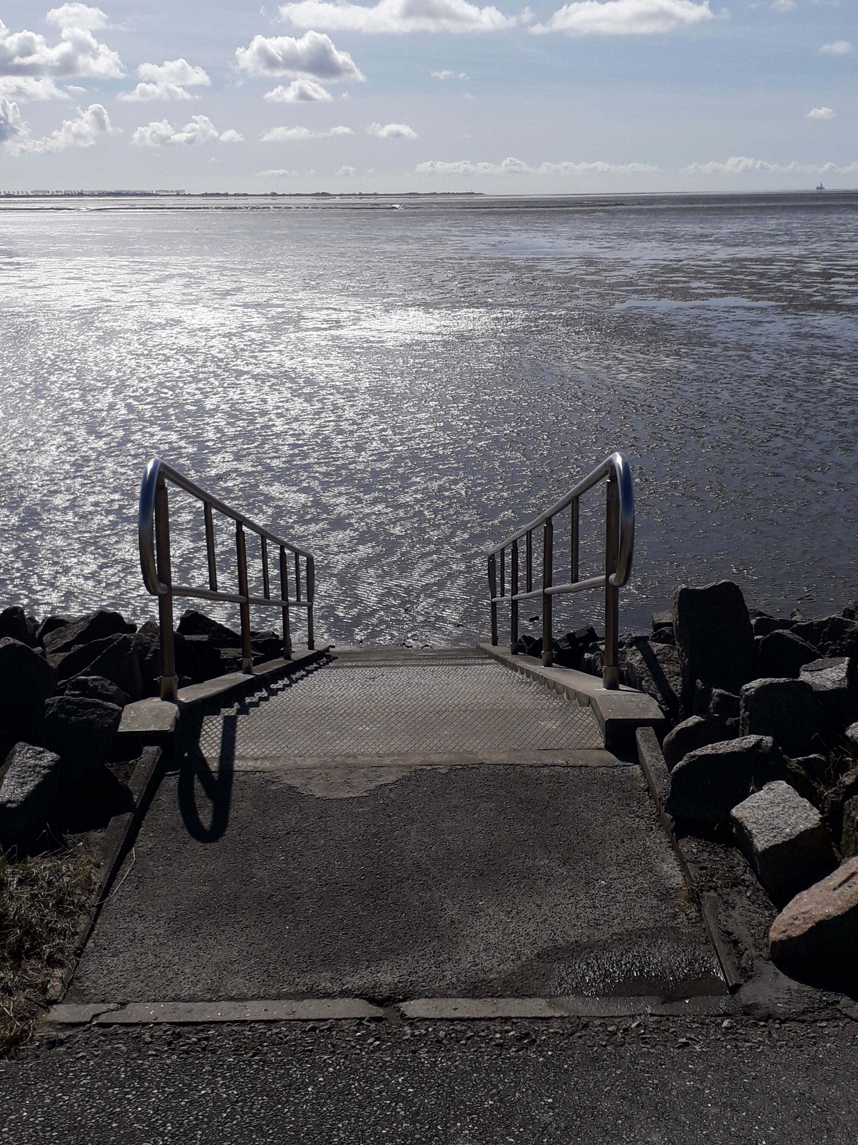 A concrete staircase leading to a body of water with metal railings, surrounded by rocks.