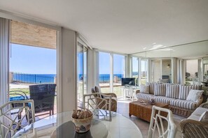 Uma sala de estar ampla com uma grande porta de vidro que dá para uma varanda, um conjunto de sofás e uma mesa de centro.