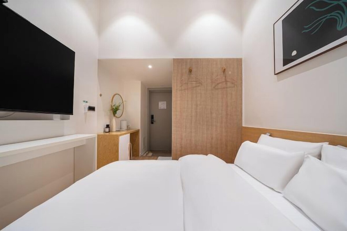A hotel room with a large bed, a TV mounted on the wall, a desk with a mirror, and a door leading to another room.
