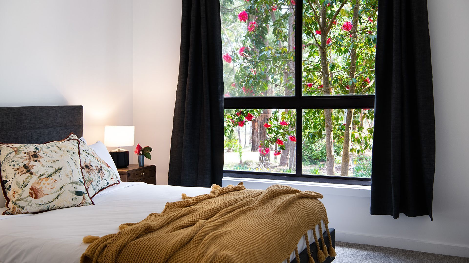 Een slaapkamer met een bed, nachtkastje, lamp en een raam met gordijnen.