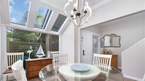 Un comedor con mesa de vidrio, sillas blancas, un aparador de madera, una araña y vistas amplias por ventanas grandes.