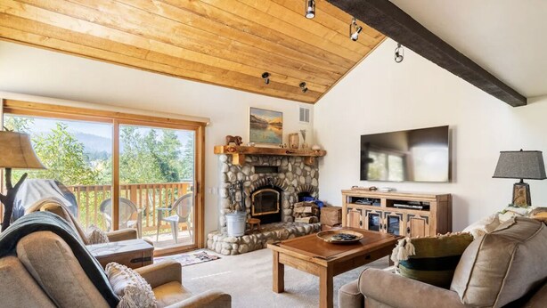 A cozy living room with a stone fireplace, comfortable seating, a flat-screen TV, and a wooden ceiling.