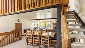A spacious dining area with a wooden table and chairs, a staircase with wooden railings, and a view of the outdoors.