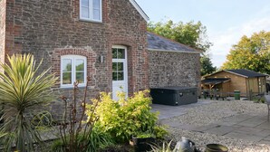A stone building with a sloped roof, a small attached wooden structure, and a gravel patio with potted plants.