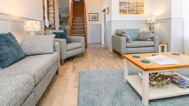 A cozy living room with two grey sofas, a wooden coffee table, and a staircase leading to an upper floor.