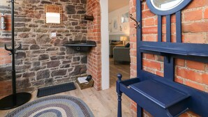 A stone wall interior with a blue-framed mirror, a black coat rack, and a small shelf.