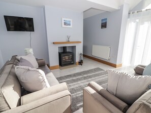 A living room with a sofa, a fireplace, a TV mounted on the wall, and a radiator. - Avalon (Pembroke)