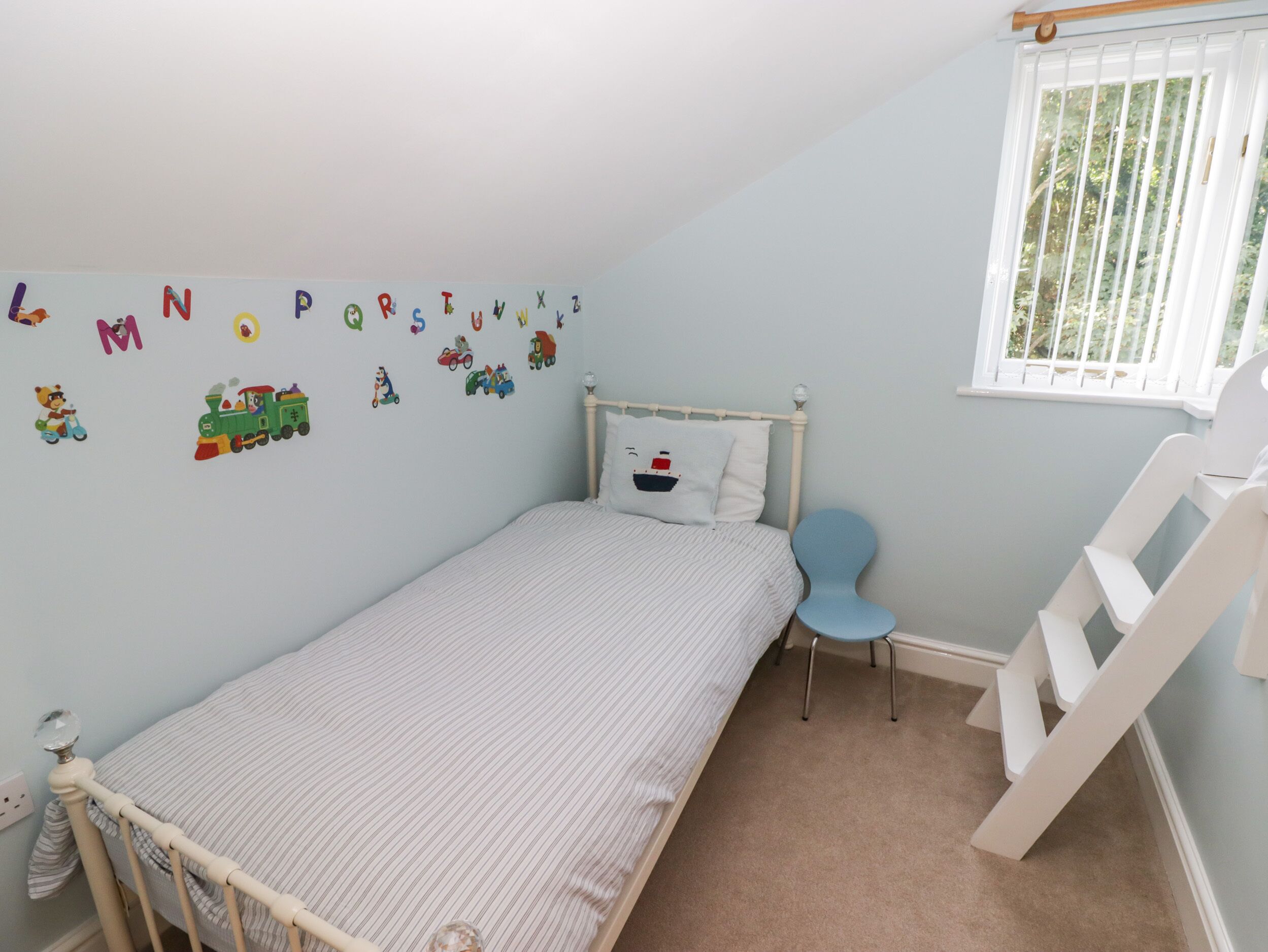 Ein Kinderzimmer mit Bett, Stuhl, Fenster und Wandstickern mit Buchstaben.