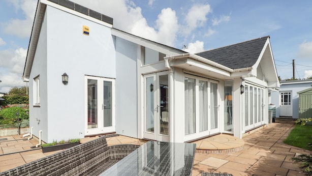 Et moderne hus med en glasindkapslet patio, spisebord og fletningsmøbler.