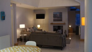 En moderne stue med en sofa, et tv ophængt på væggen, en pejs og et lille sofabord med en lampe.