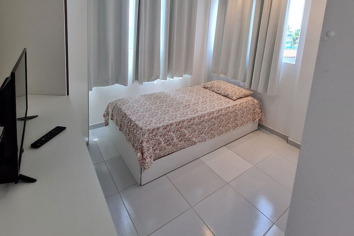 A bedroom with a bed, curtains, a TV, and a window.