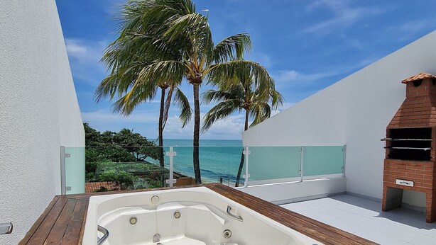 A hot tub on a wooden deck with a view of the ocean and palm trees.