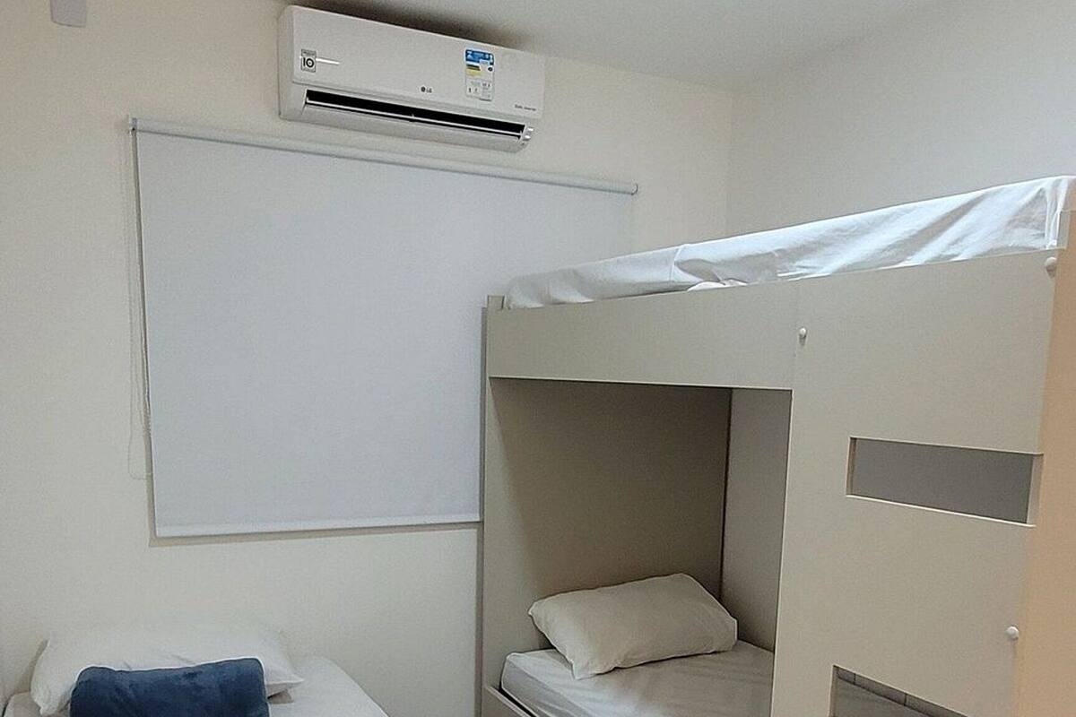 A bunk bed room with a white bed, a blue pillow, a white mattress, and a white wall.
