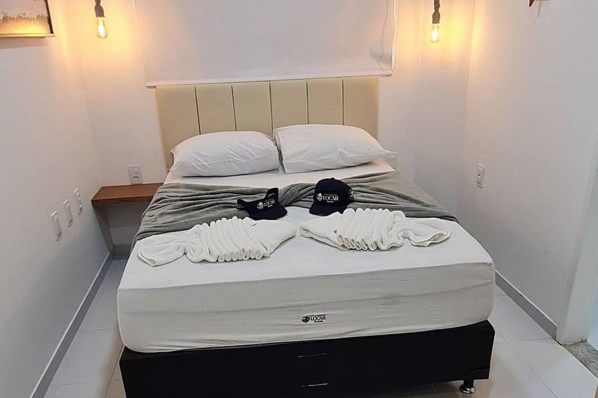 A neatly made bed with a white mattress and a black base, a white wall-mounted air conditioner, and a ceiling light.