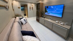 A modern living room with a beige sofa, a flat-screen TV mounted on the wall, and a wooden cabinet below.