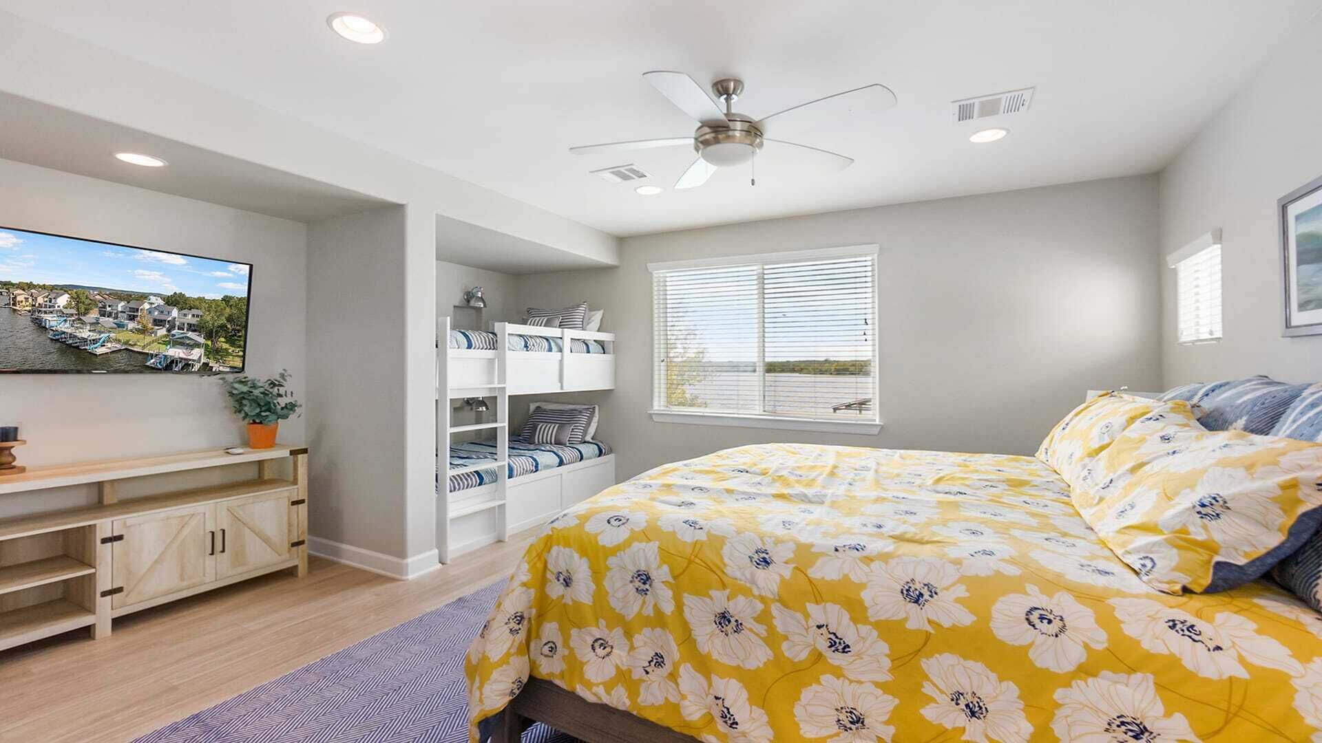 A bedroom with a bed, a ceiling fan, built-in shelves, a window, and a TV on the wall.