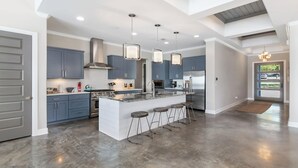 A modern kitchen with a central island, bar stools, stainless steel appliances, and pendant lighting. - Bud Bliss Retreat | Concierge Services (Kingsland)