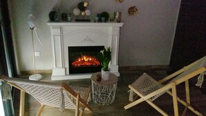 A cozy living room with a fireplace, two wooden chairs, a small side table, and decorative items on the mantel. - Spa Privatif Jacuzzi et Sauna, Maison de Ville 4 Personnes (Yerville)