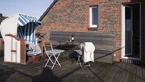 Eine Terrasse mit einer Ziegelwand, einer Holzbank, einem Tisch mit einer Weinflasche und einem gestreiften Sonnenschirm.