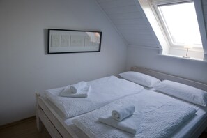 A bedroom with a sloped ceiling, a skylight, a framed picture on the wall, and neatly made beds with rolled towels.