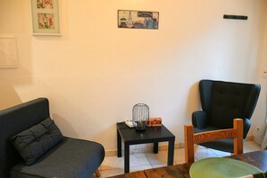 A living room with a sofa, a chair, a small table with a decorative item, and a welcome sign on the wall. - Apartment 'Villa Les Lauriers' with Shared Terrace, Wi-Fi and Air Conditioning (Lioux)