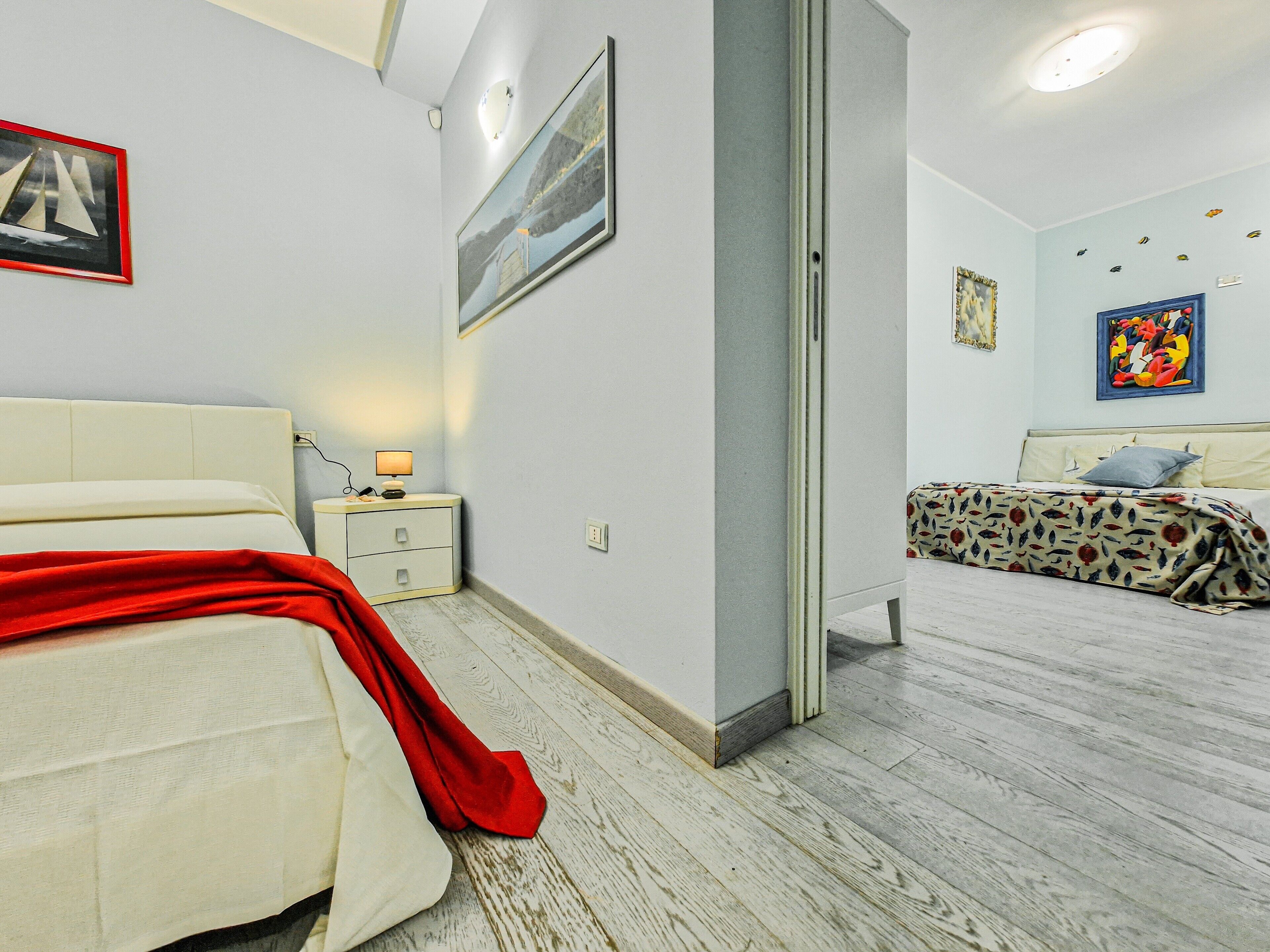 A bedroom with a bed, a nightstand, a lamp, and a door leading to another room.