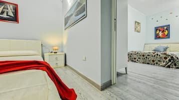 A bedroom with a bed, a nightstand, a lamp, and a door leading to another room.