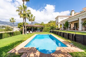 A swimming pool with a pergola, palm trees, and a view of mountains.