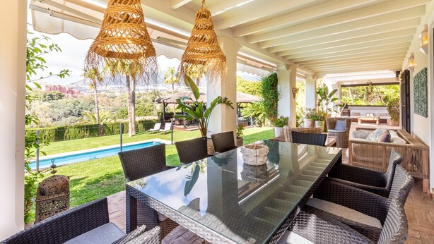 An outdoor dining area with wicker furniture, hanging rattan lamps, and a view of a pool and greenery. - 'Luxury Villa Larios Torrequebrada' with Sea View, Pool & Wi-Fi (Benalmádena)
