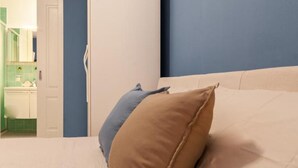 Ein Schlafzimmer mit einem Bett, Kissen, einer Tür und einem durch eine offene Tür einsehbarer Badezimmer.
