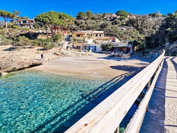 A coastal area with clear water, a wooden walkway, and buildings on a hillside.