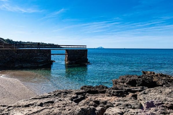 Un puente costero sobre el agua, con una costa rocosa y cielo despejado.