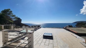 Una terraza en la azotea con vista al mar, una baranda de metal y un objeto rectangular pequeño en el suelo.