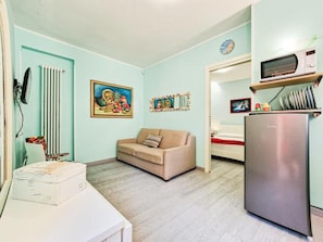Un espacio habitable pequeño con kitchenette, sofá y refrigerador.