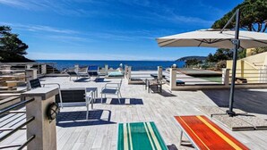 Eine Terrasse mit Liegestühlen und Sonnenschirmen mit Blick auf ein Gewässer.