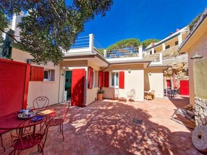 A courtyard with a dining area, red shutters, and a stone wall.