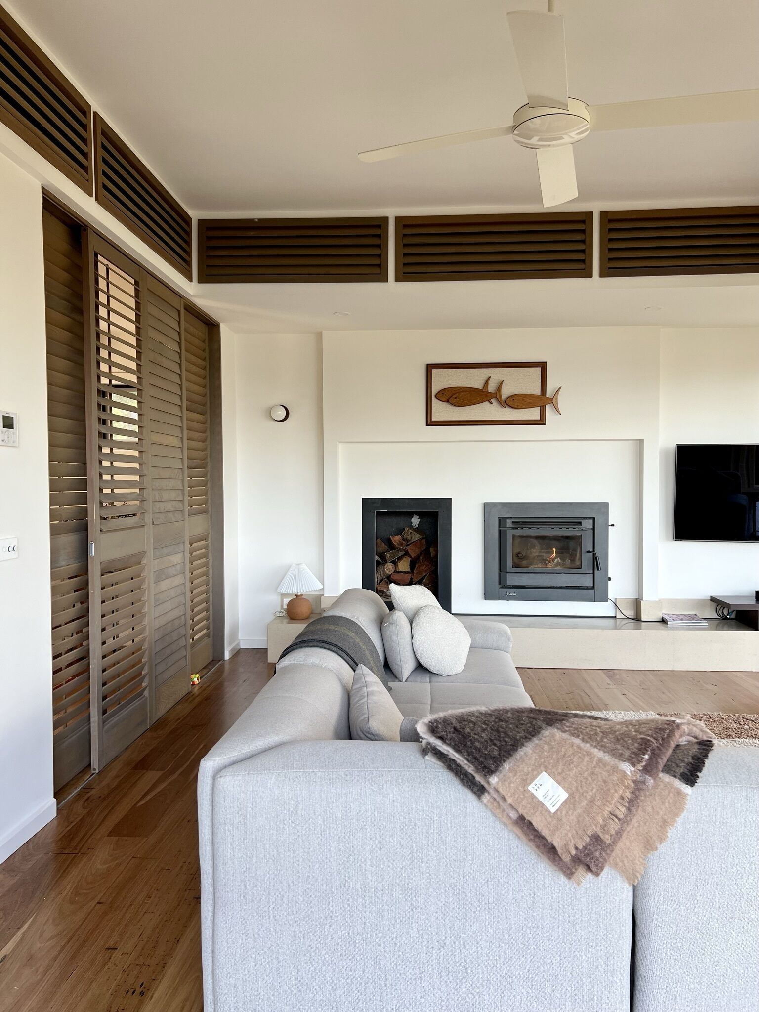 Een moderne woonkamer met een grijze bank, een open haard en een plafondventilator.