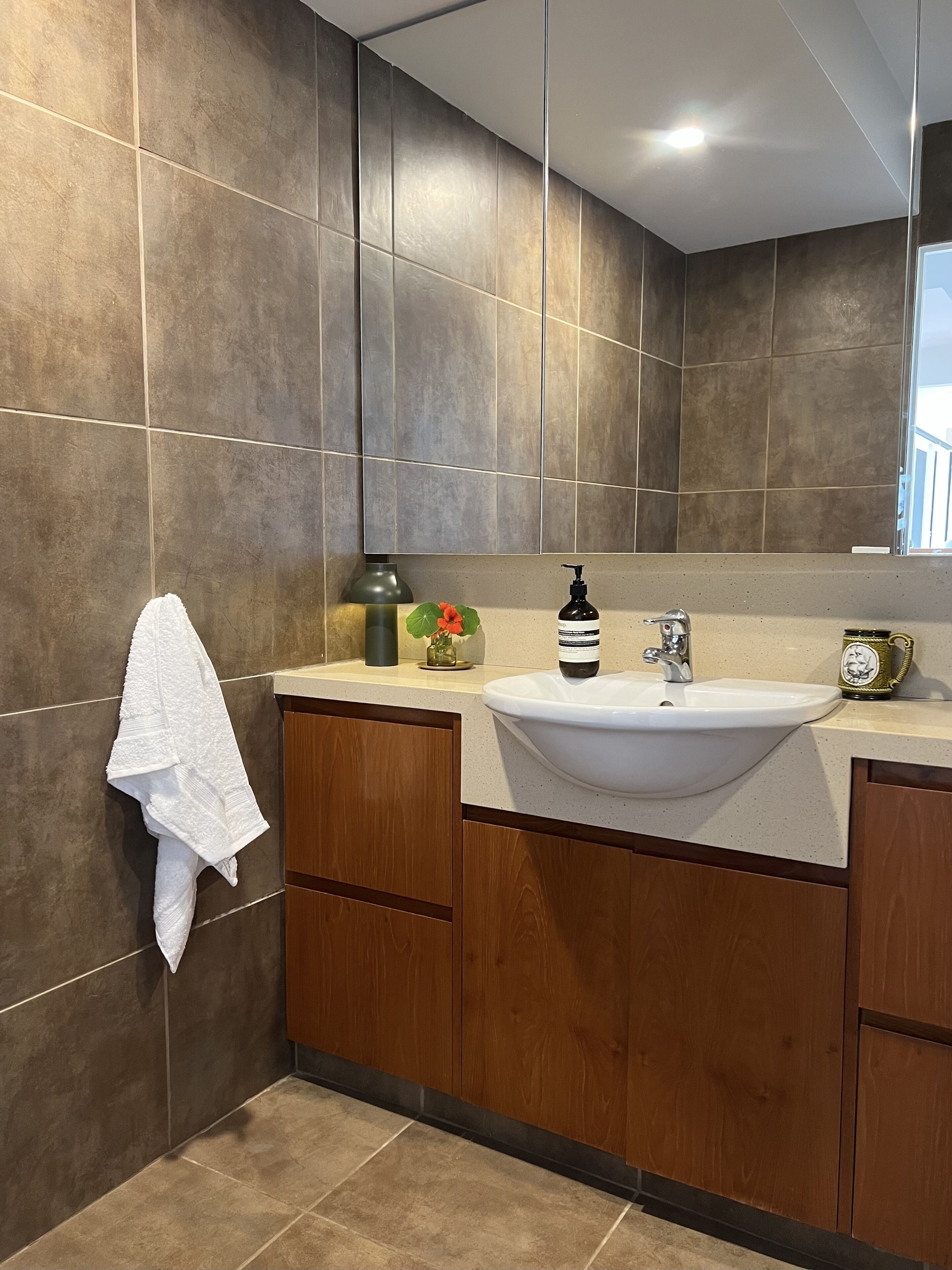 A modern bathroom with a large sink, wooden cabinets, and a towel hanging on the wall.