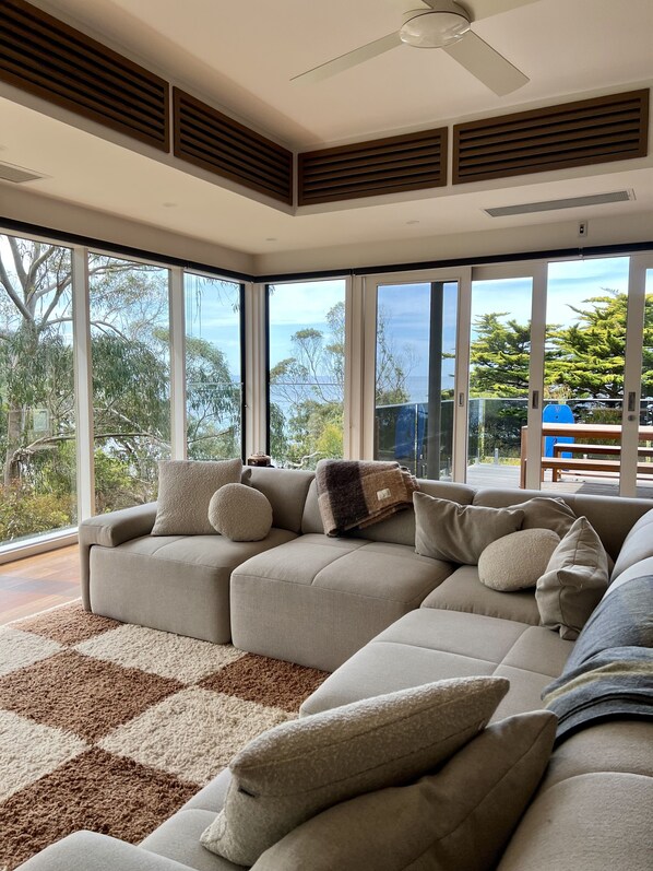Una sala moderna con un sofá seccional, ventanas amplias y vistas al exterior.